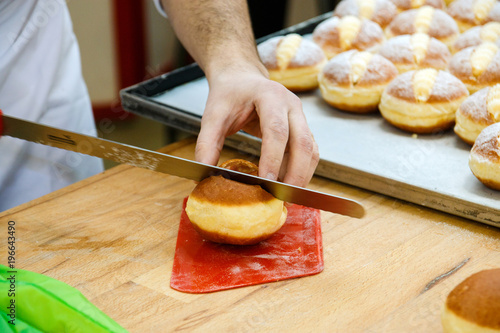 Canvas Print pastry chef cuts a bun with a knife to fill it with cream