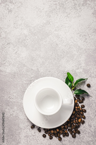 Empty white cup and coffee beans on concrete background. Top view, space for text.