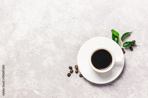 Black strong coffee in white cup, coffee beans and leaves on concrete background. Top view, space for text.