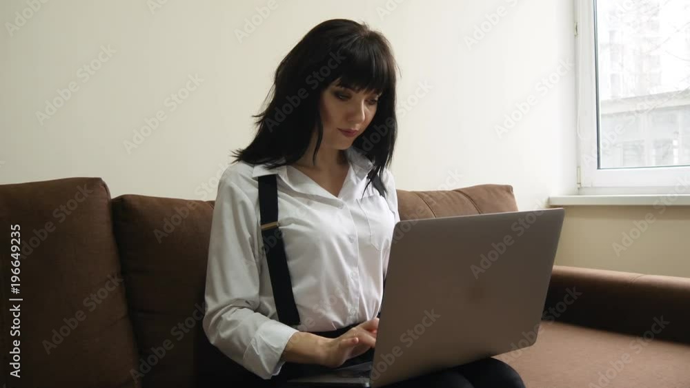 Young pretty woman using laptop. Smiling girl sitting on sofa relaxing while browsing online shopping website on laptop. Happy girl browsing through the internet during free time at home. Young pretty woman using laptop. Smiling girl sitting on sofa relaxing while browsing online shopping website on laptop. Happy girl browsing through the internet during free time at home.