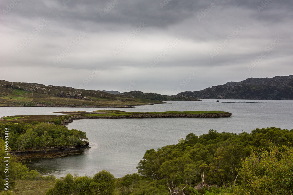 Balgy, Scotland - June 10, 2012: Silver colored Upper Loch Torriden with wide and far view under gray cloudscape. Green hills with trees in front. Mountains on horizon.