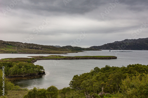 Balgy, Scotland - June 10, 2012: Silver colored Upper Loch Torriden with wide and far view under gray cloudscape. Green hills with trees in front. Mountains on horizon. © Klodien
