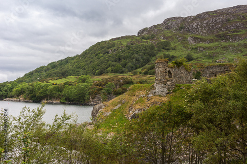 Stromeferry  Scotland - June 10  2012  Castle Strome ruins on green shore cliff over Loch Carron. Cloudscape and forested mountain in back. Top of trees in front.