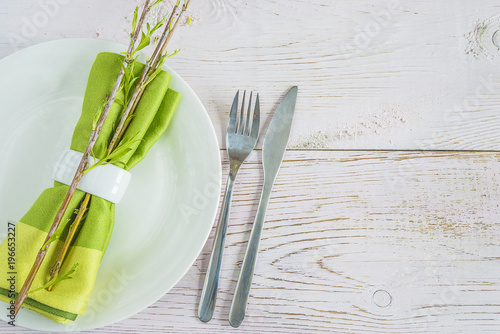 Table setting with white plate  cutlery  green napkin with ring and willow twigs with young leaves