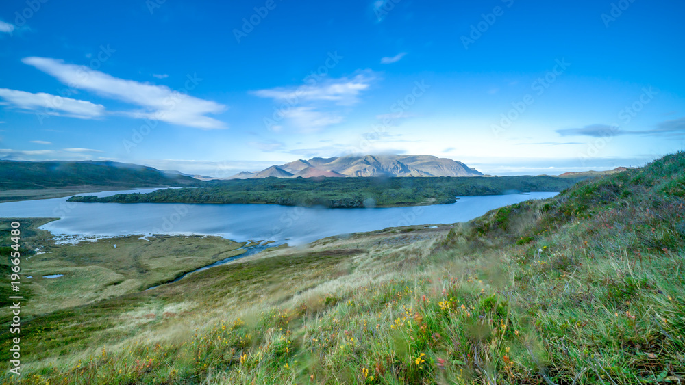 Landscape photography of a mountain in Iceland having smooth running river in foreground with green autumn grass meadow