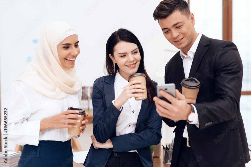 Two women and a man are drinking coffee and watching something on the phone screen. Two women and a man are drinking coffee and watching something on the phone screen.