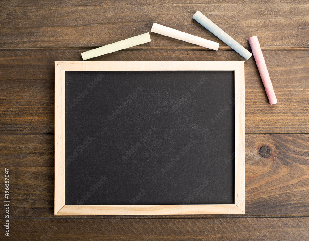 Top view of chalkboard next to colored chalk on brown wooden table. Copy space. Top view of chalkboard next to colored chalk on brown wooden table. Copy space.