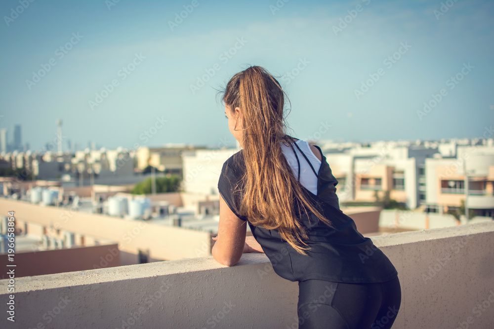 Back view of young woman with ponytail looking at city view.