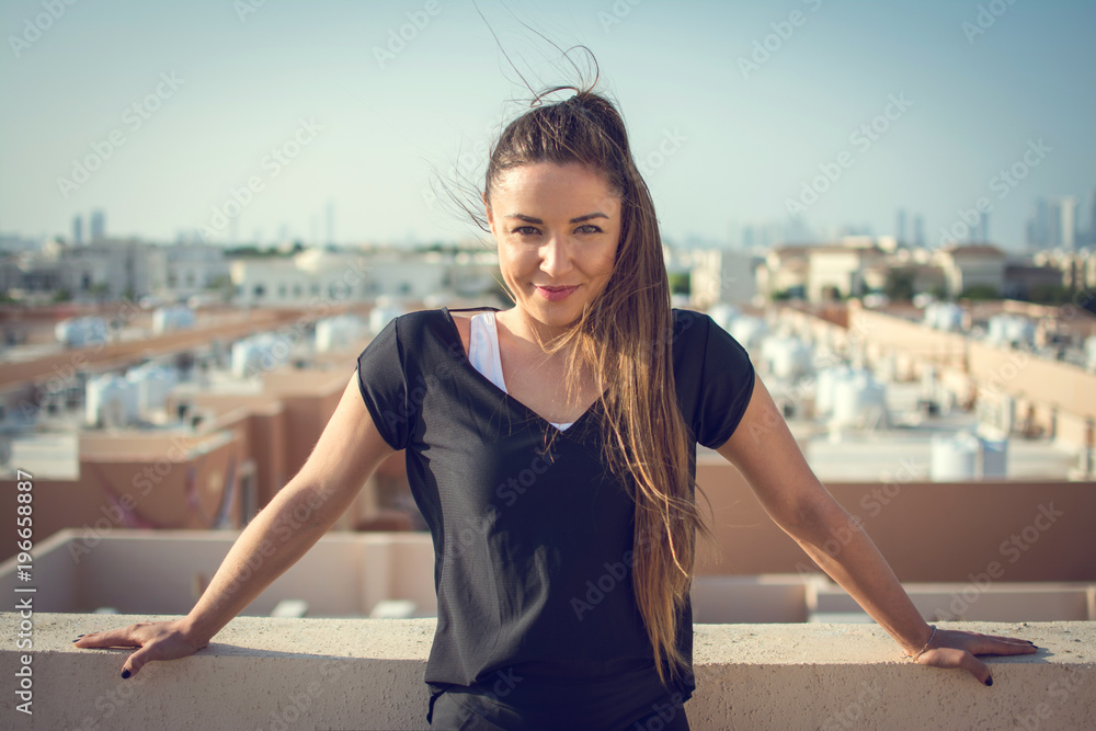 Fototapeta premium Portrait of beautiful smiling young woman posing on rooftop with a city view in the background.