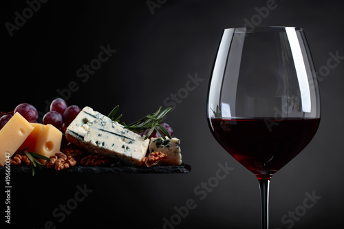 Glass of red wine with various cheeses , grapes and walnuts .