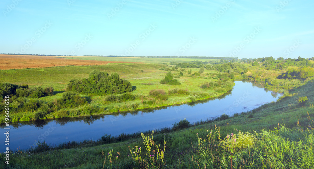 Sunny summer landscape.Green hills,fields and meadows.River Upa in Tula region,Russia.Sunrise.Quiet stream.Calm.Warm sunlight.Cloudless clear bright blue sky. 