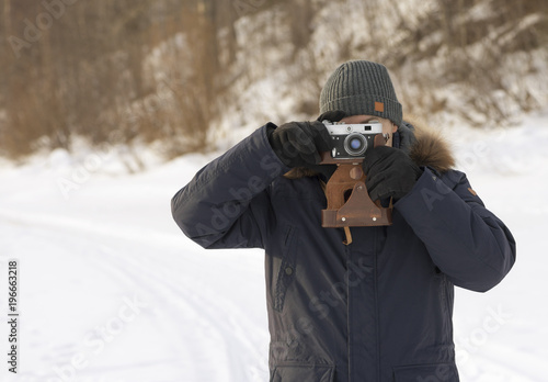 The man is taking pictures outdoors in a park. The retro photo camera is in male hands. The European is on a walk in winter jacket. It is photographing in nature.