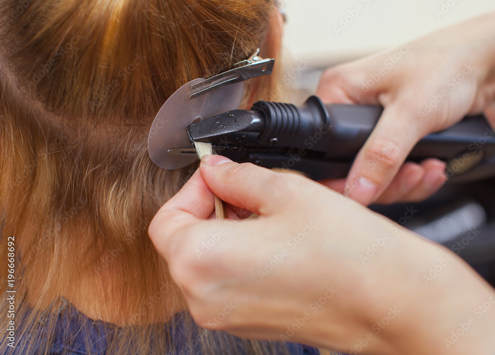 The hairdresser does hair extensions to a young girl, a blonde in a beauty salon. Professional hair care. The hairdresser does hair extensions to a young girl, a blonde in a beauty salon. Professional hair care.