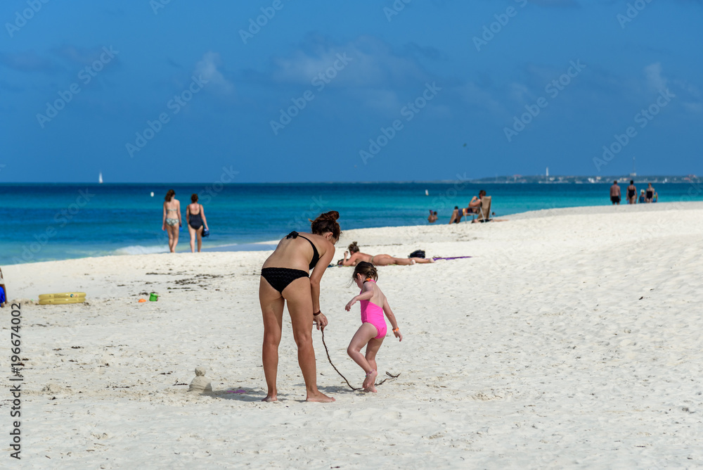 A mother plays with her baby girl by the sea in the beautiful Eagle Beach in Aruba.