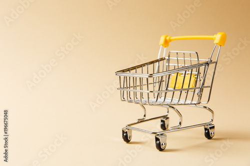 Close up of supermarket grocery push cart for shopping with black wheels and yellow plastic elements on handle isolated on beige background. Concept of shopping. Copy space for advertisement