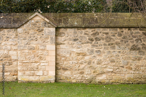 Closeup of yellow and gray stone wall, the green grass and trees behind for background.