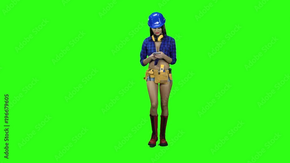 Girl in shorts and a helmet is picking sms on the phone against a green background Girl in shorts and a helmet is picking sms on the phone against a green background