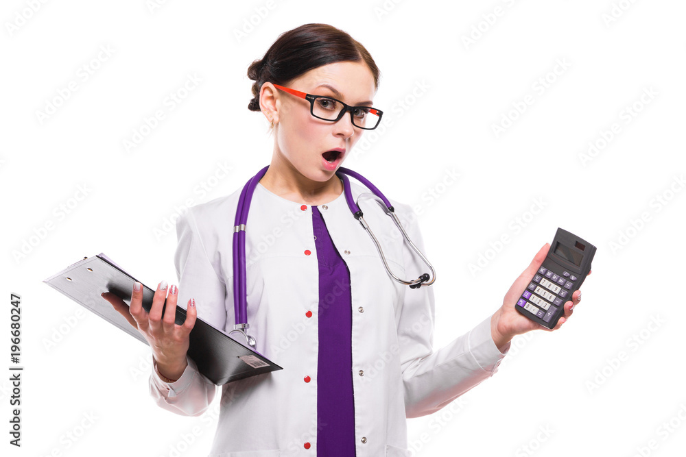 Young beautiful female doctor holding clipboard and showing calculator in her hands on white background Young beautiful female doctor holding clipboard and showing calculator in her hands on white background