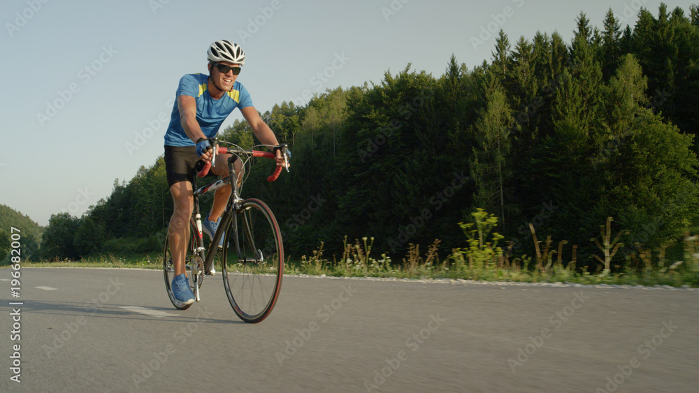 LOW ANGLE: Young male biker pedals along empty asphalt road on summer afternoon.