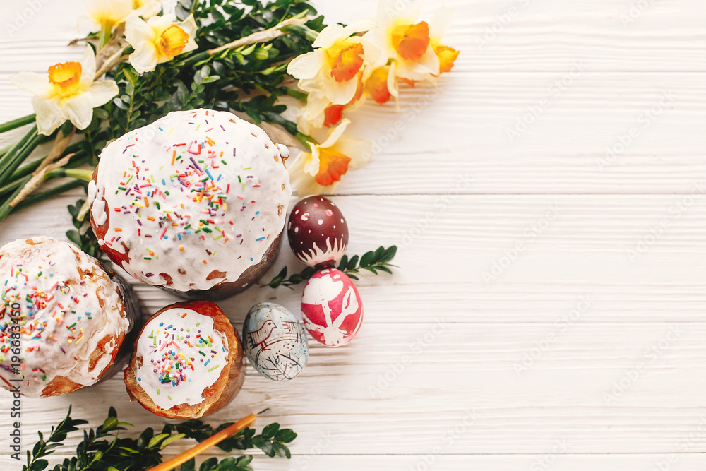delicious easter cake with colorful icing and eggs on white rustic wooden background with spring flowers and candle. space for text. happy Easter concept, flat lay. seasons greetings