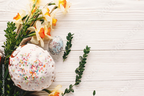 happy Easter concept. stylish painted egg and easter cake on white rustic wooden background with spring flowers. seasons greetings card. space for text. modern easter flat lay
