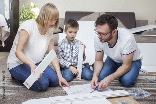 Obraz na płótnie Tata mama i synek spędzają wspólnie wolny czas skręcając własnoręcznie meble. Mama trzyma w rękach białe długie elementy w salonie