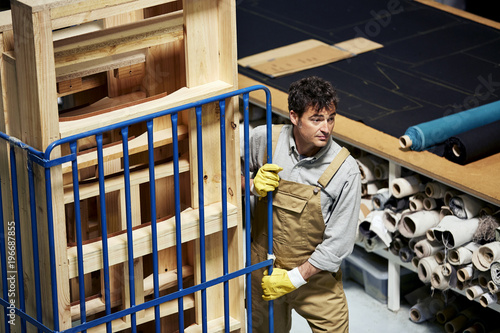 Worker Pulling Trolley With Stacked Wooden Frames In Sofa Worksh photo