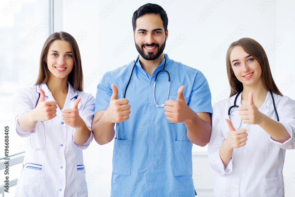 Successful team of medical doctors are looking at camera and smiling while standing in hospital Successful team of medical doctors are looking at camera and smiling while standing in hospital