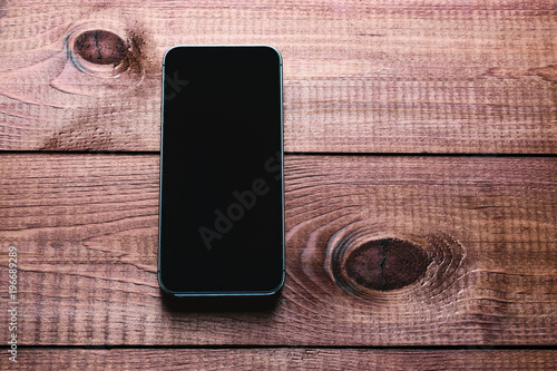 Top view of a modern smartphone with large screen on vintage wooden table. Blank empty display. Mock up