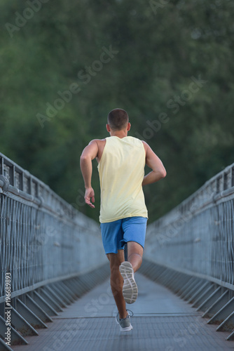Anonymous sporty man jogging on pedestrian bridge outdoor