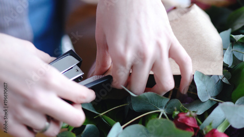 Florist using stapler to attach a craft paper. Close up view of arranging bouquet
