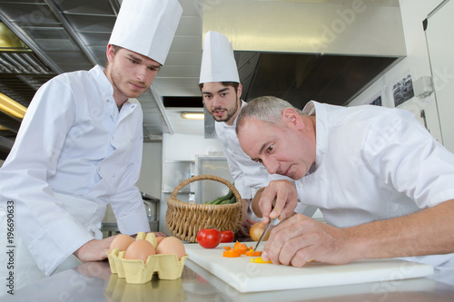 apprentices watching chief chef garnishing a dish
