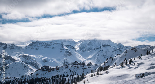 Panorama over snowy hills in the alps. Winter landscape. Low clouds or myst is covering the top of the moutains.