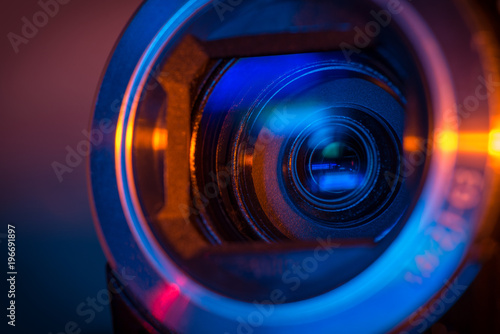 Video camera lens closeup lit by blue and orange neon light