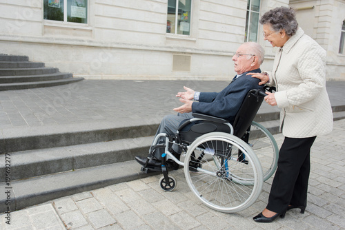 old man on wheelchair and woman carrying him © auremar