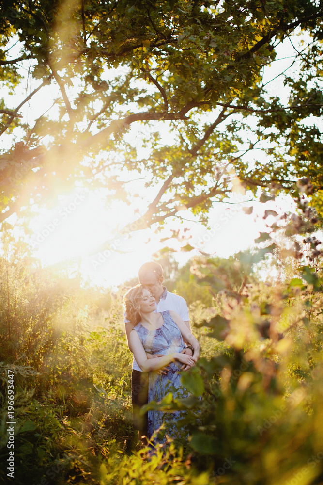 Dreamy portrait of young family with pregnant woman standing in sunset light Dreamy portrait of young family with pregnant woman standing in sunset light