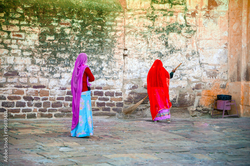 Two indian women are cleaning the stone antique street with broom in India photo