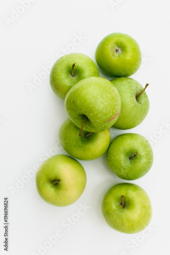 Flatlay with eight fresh, green-yellow Golden Smith or Granny Smith apples on white background