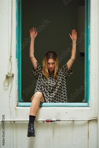Girl in unglazed window with arms up and leg over frame. photo