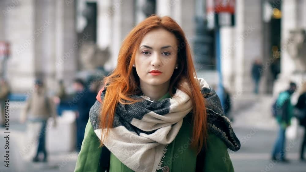 Serious red haired woman lokking to the camera in the street Serious red haired woman lokking to the camera in the street