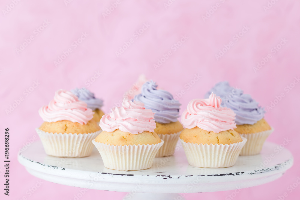 Cupcakes decorated with violet and pink buttercream on shabby shic stand on pastel pink background