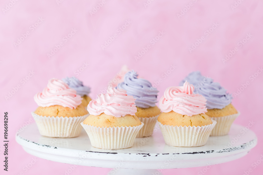Cupcakes decorated with violet and pink buttercream on shabby shic stand on pastel pink background Cupcakes decorated with violet and pink buttercream on shabby shic stand on pastel pink background