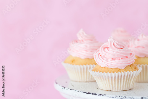 Cupcake decorated with pink buttercream on shabby shic stand on pastel beautiful pink background.