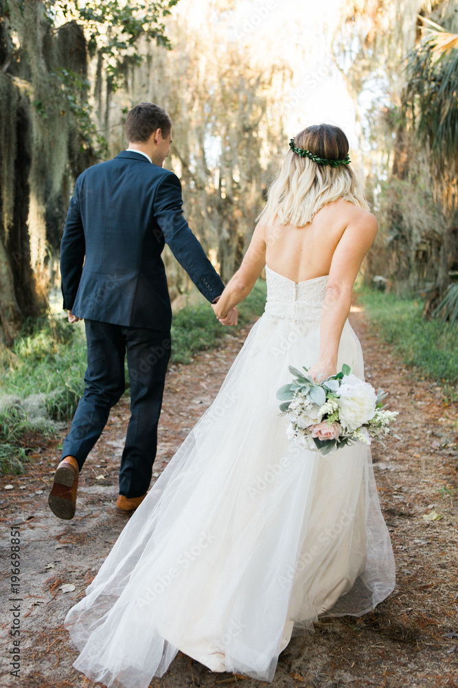 Back view of bride and groom holding hands and walking in outdoors ...