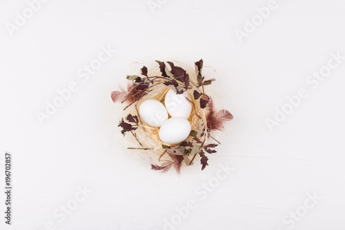 White eggs in stylish straw nest decorated with leaves and feathers. Isolated on white background. Flat lay, top view. Easter concept.