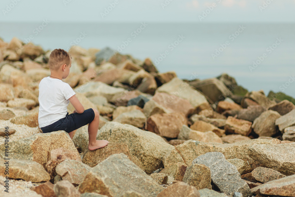 Boy sitting on rocks near sea shore waiting