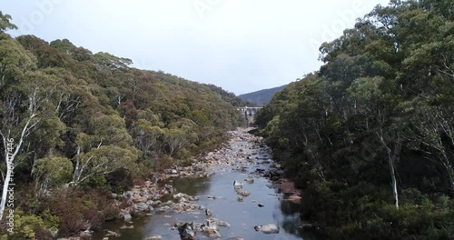 Gughega hydro dam on Snowy river high in Snowy mountains of NSW, Australia, during winter rainy weather flying over stony riverbed between evergreen gum trees.
 photo