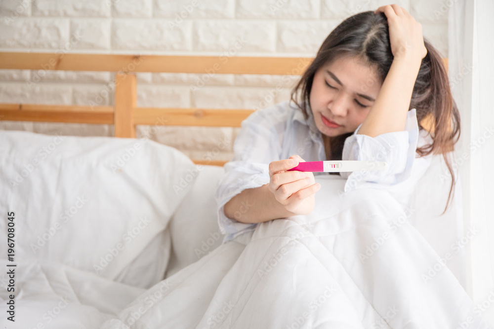 Selective focus Pregnancy test positive result on hand of woman sitting on bed in her bedroom. Pregnancy is not ready concept. Selective focus Pregnancy test positive result on hand of woman sitting on bed in her bedroom. Pregnancy is not ready concept.