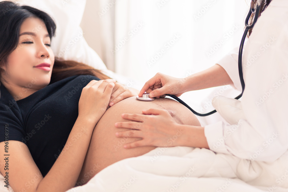 Obraz premium Female Obstetrician doctor with stethoscope listening to pregnant woman baby heartbeat at hospital.