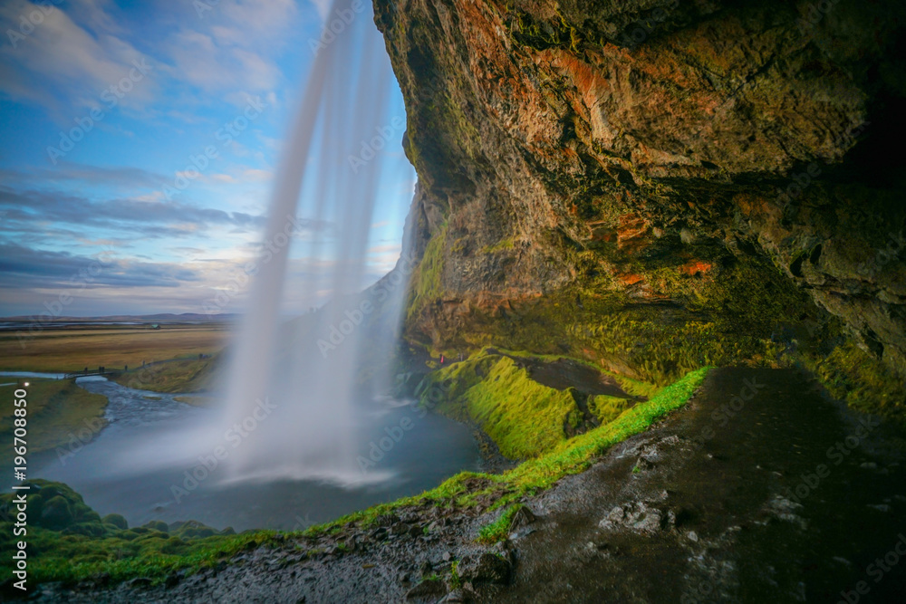 Big cave behind The Seljalandsfoss waterfall in Iceland with beautiful evening sky as background